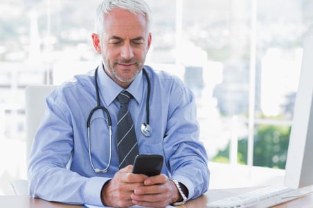 Doctor using his smartphone in the office at desk